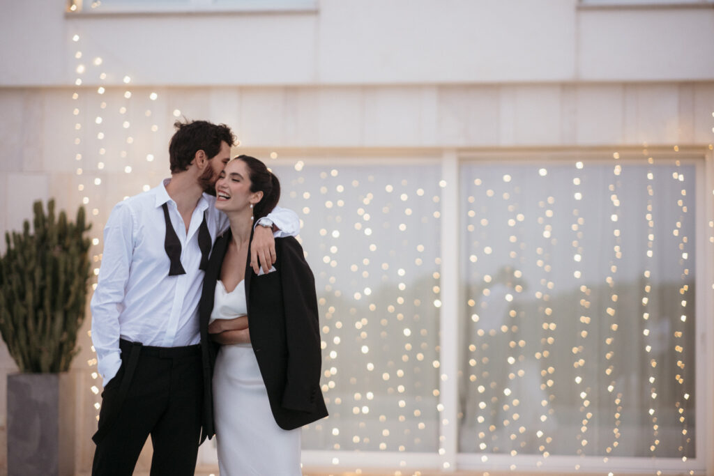 fraeuleinseelig.de_Mallorca-Hochzeit in einer Finca240416_19 Hochzeitspaar umarmt sich vor einem Lichtervorhang am Abend